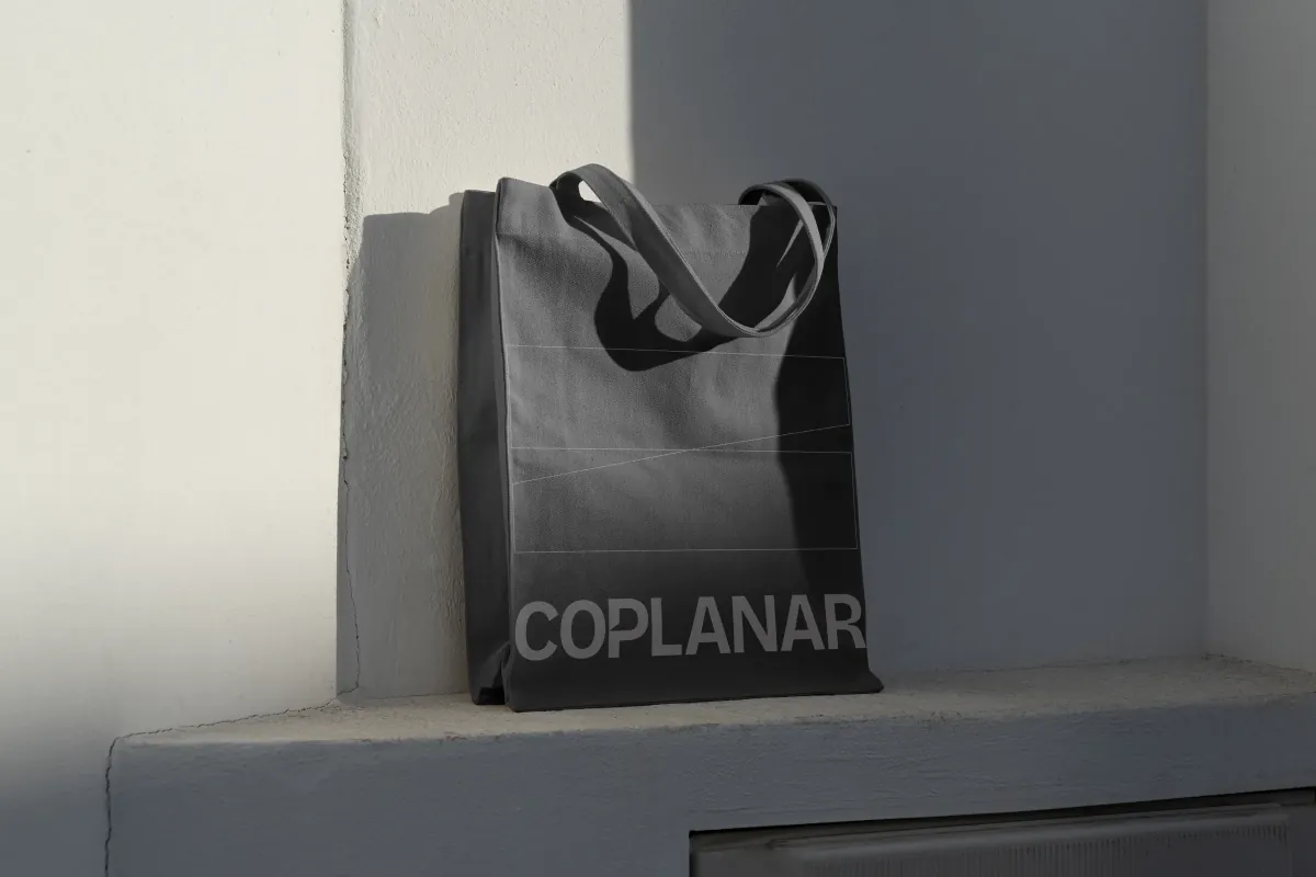 Coplanar tote bag with the wordmark, photographed against concrete